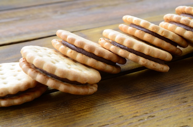 A round sandwich cookie with coconut filling lies in large quantities on a brown wooden surface.