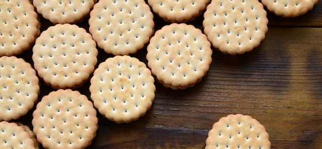 A round sandwich cookie with coconut filling lies in large quantities on a brown wooden surface