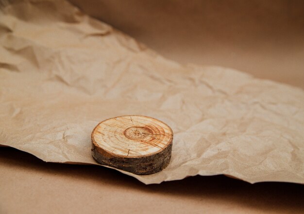 A round slice of wood lies on crumpled beige kraft paper. Wrapping paper for parcels and gifts. An empty space for the text. Monochrome image. A podium for products.