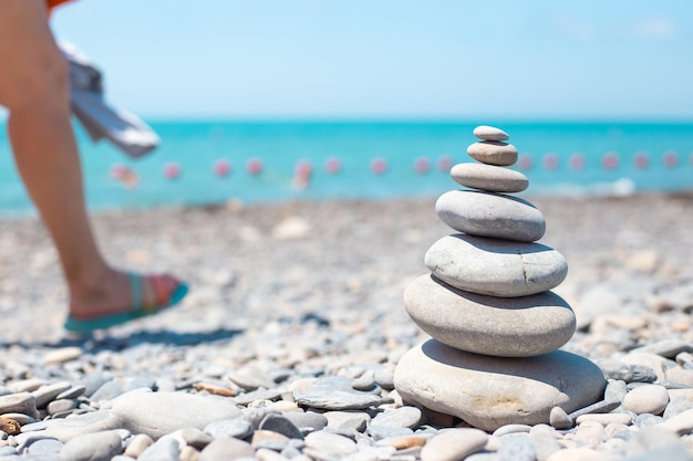 Round stones are stacked on top of each other by a pyramid on the seashore where tourists walk