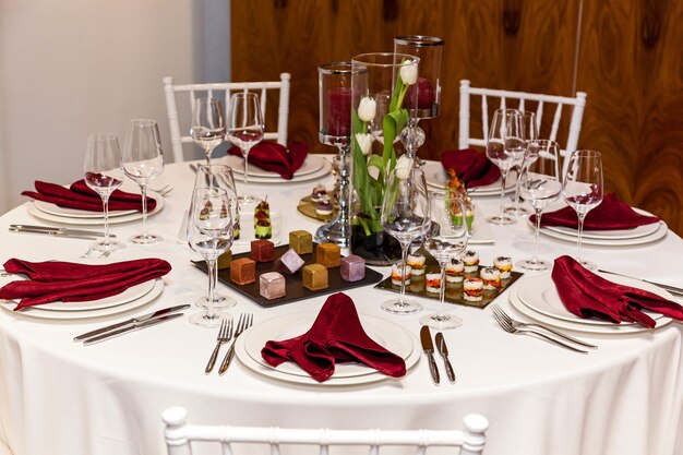 白いテーブルクロスと赤いナプキンが付いた円卓、宴会用の軽食が付いたカトラリーのセット。ケータリング、ボンケット用サーバーテーブル