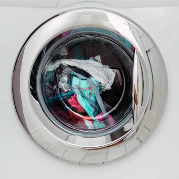 Round transparent door hatch automatic washing machine, through which you can see coloured linen.