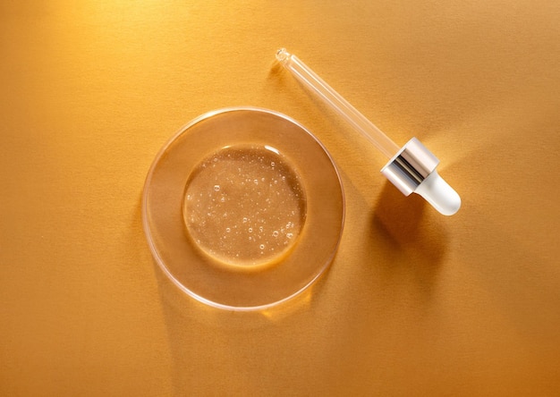 Round transparent drop of clear gel serum in petri dish on gold\
background