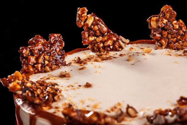 Round white cake with caramel and chocolate puffed rice on a round tray on black background