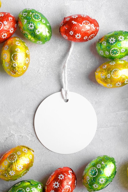 Round white Easter tag mockup with Happy Easter chocolate easter eggs on grey stone background