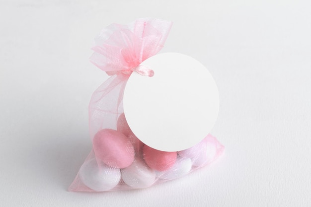 Round white tag mockup with gift with pink chocolate confetti in a bag with pink ribbon Wedding favor tag for souvenir