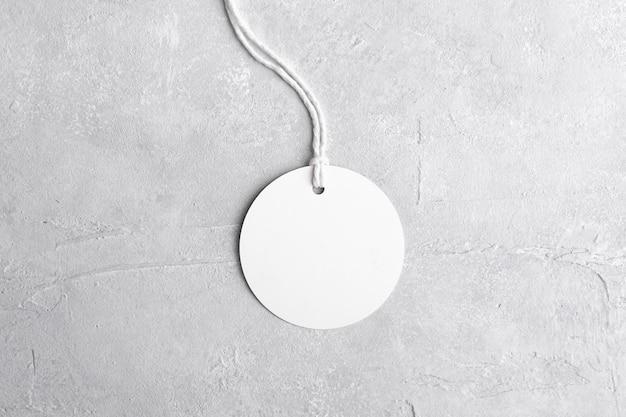 Round white tag mockup with white cord close up Blank paper price tag isolated on grey stone background with copy space