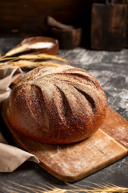 Pane intero rotondo su un tagliere di legno cosparso di farina e spighette di cereali su un tavolo scuro, foto verticale, spazio libero per il testo. foto di alta qualità