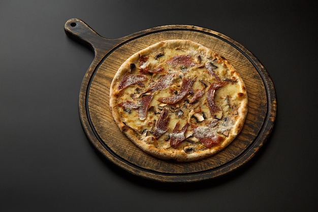 Round wooden board with pizza isolated on a black background.