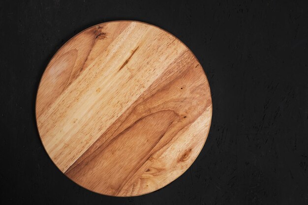 Round, wooden cutting board on a black background.