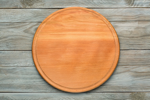 Round wooden cutting board for pizza on gray wooden table. Mockup for food project. Top view.