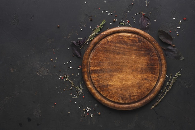 Round wooden plate with herbs and salt on dark wooden background top view