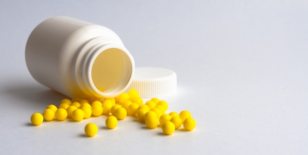 Round yellow vitamins are poured out on a white glossy table from a white plastic bottle. Concept. Place for the label. Diagnosis.