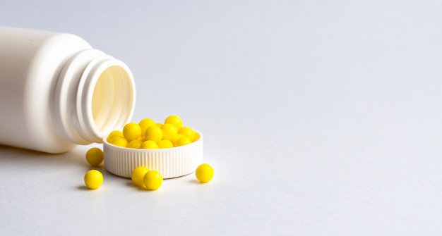 Round yellow vitamins are poured out on a white glossy table from a white plastic bottle. Concept. Place for the label. Diagnosis.