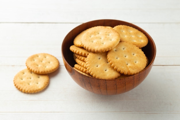 Rounded cracker cookies in a wooden bowl on white wooden table background.