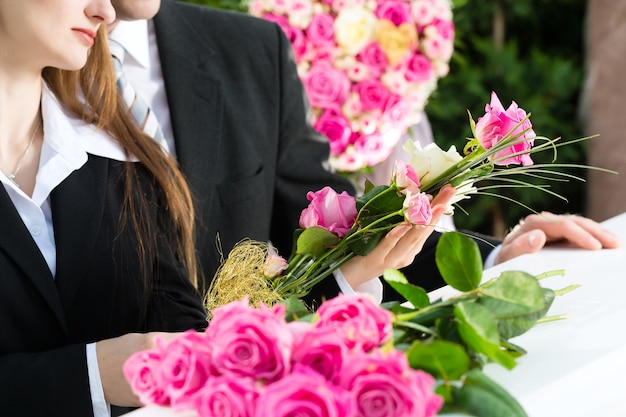 Rouwende man en vrouw op begrafenis met roze roos die zich bij kist of kist bevindt