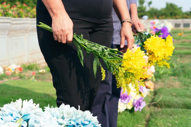 Rouwpaar dat bloemen in handen houdt en bij graf op begraafplaats staat. Paar in zwarte kleren op begraafplaats.