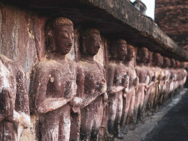 Row of ancient stucco, praying buddha statue at the base of old pagoda at Wat Mahathat Temple in the precinct of Sukhothai Historical Park, a UNESCO World Heritage Site in Thailand, close up.