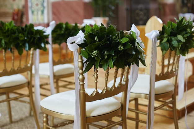 Row of chairs decorated with green leaves and white ribbons for wedding ceremony