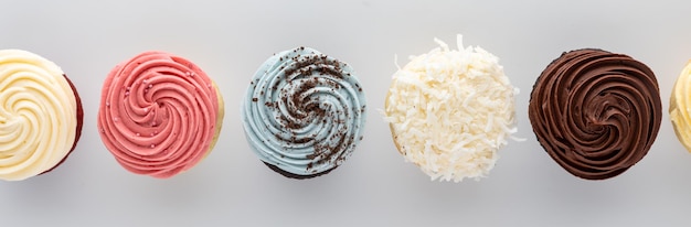 a row of decorated icing top cupcakes against a light background