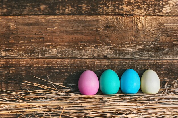 Photo a row of eggs on a straw near a wooden wall. concept on the theme of easter.