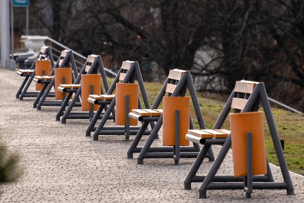 Fila di nuove panche di legno vuote e bidoni della spazzatura su un marciapiede in un parco cittadino.
