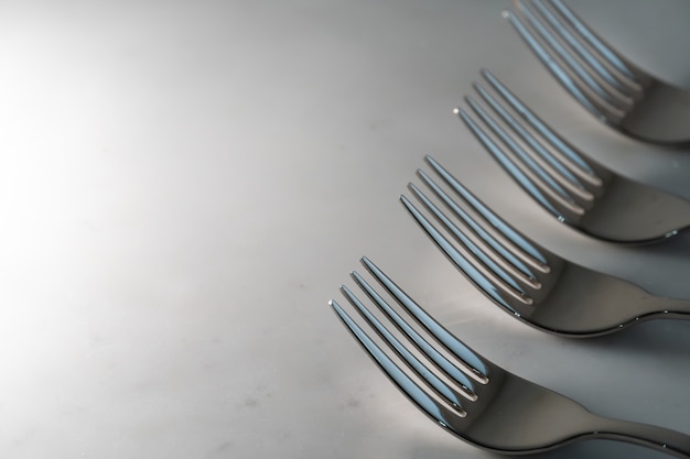 Row of Forks on white marble texture background. Concept for food and dining tableware