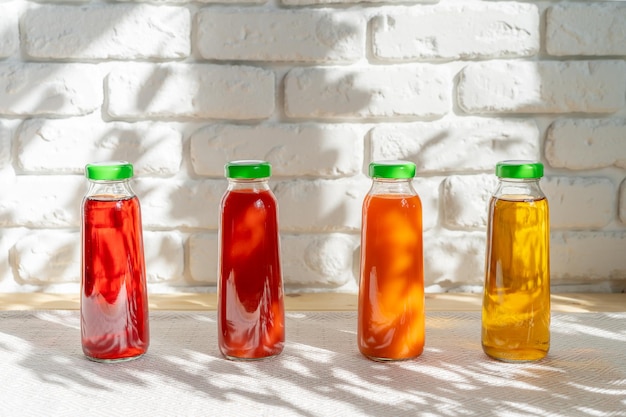 Row of glass bottles of different juices against white brick wall