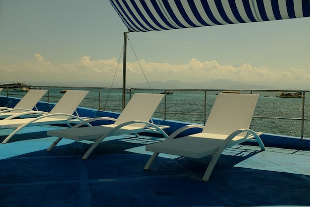 A row of lounge chairs on a boat with a blue and white striped cover.