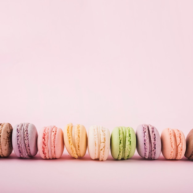 Row of many colorful delicious macaroons on pink background