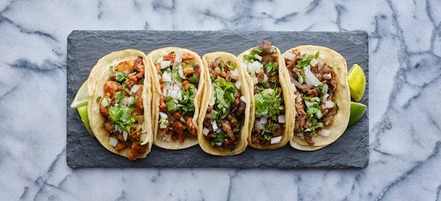 Row of mexican street tacos on slate with carne asada and al pastor in corn tortilla