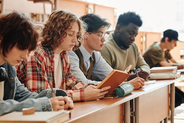 講義で机のそばに座っている大学の多文化の十代の学生の列