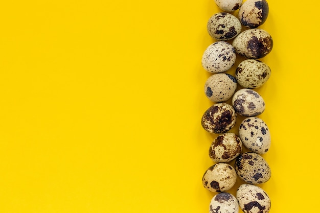 Row quail eggs on yellow paper background. top view copy space