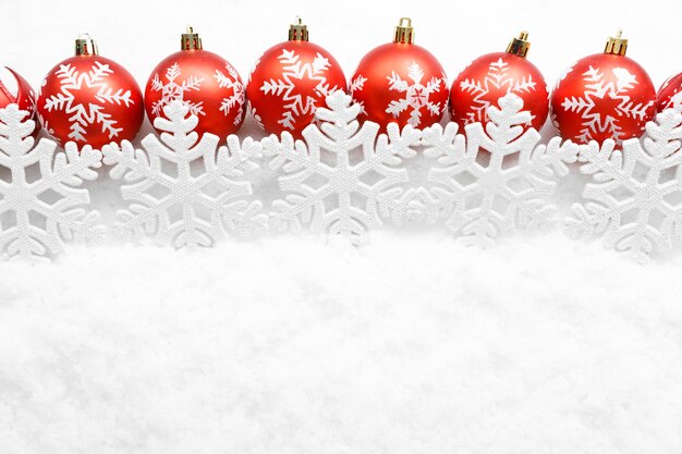 Row of red christmas balls with snowflakes on white snow background