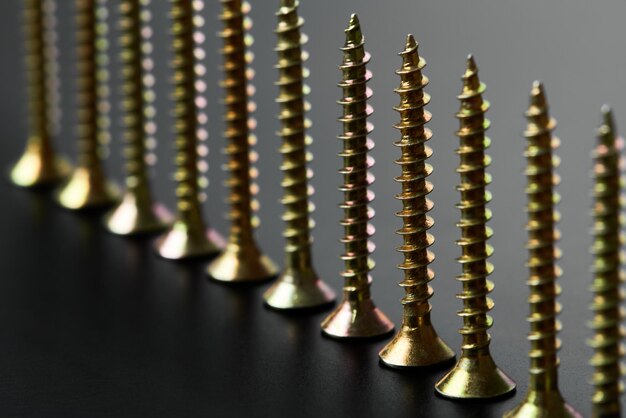 A row of screws or selftapping screws with a yellow coating on a black background