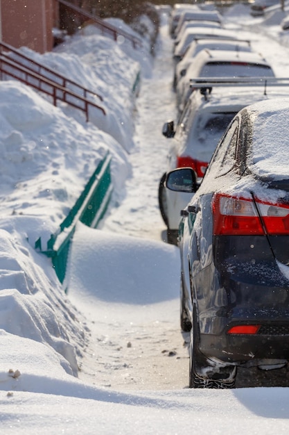 Row of snow drifted cars in a row along the street near residential building at winter day snowfall