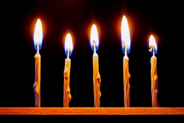 A row of thin candles are burning on a black background