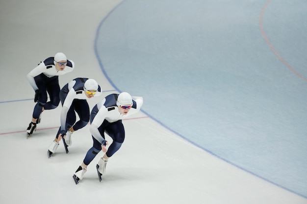 スポーツ ユニフォームを着た 3 人の選手の列がアイス スケート リンクを前方に滑る