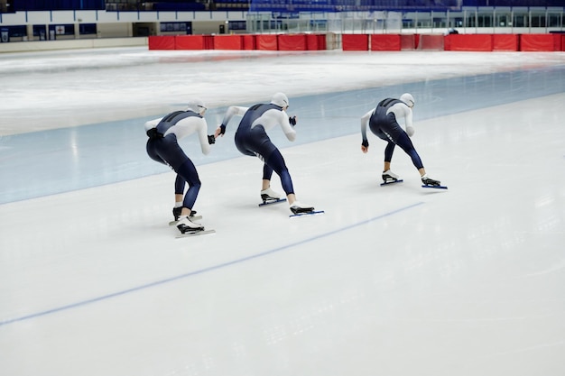 Row of three young sportsmen in uniform moving along skating rink