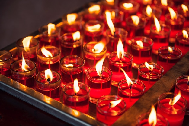 Row of votive religious red candle with flame in glass at chinese temple