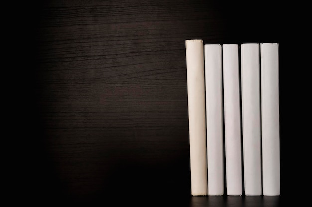 A row of white blank books on a shelf on a black background, free space for copying, without labels, an empty spine. Back to school. Education