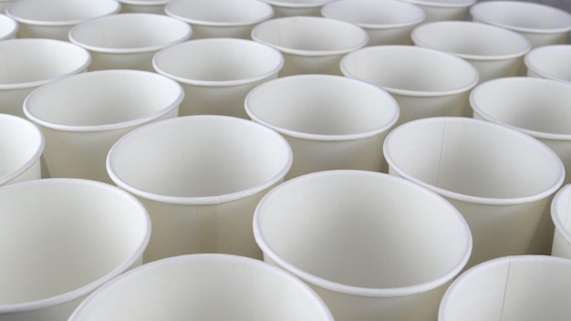 Row of white disposable eco friendly paper cup for coffee or hot beverage on dark backdrop