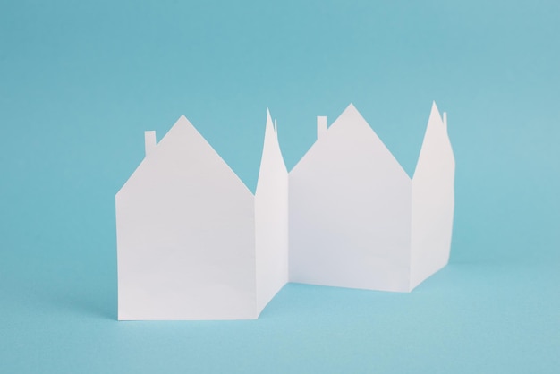 Photo row of white paper houses on a blue colored background, empty copy space, symbol real estate