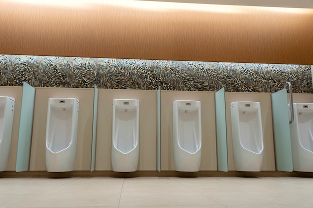 A row of white urinals in tiled wall in a public restroom. Empty man toilet