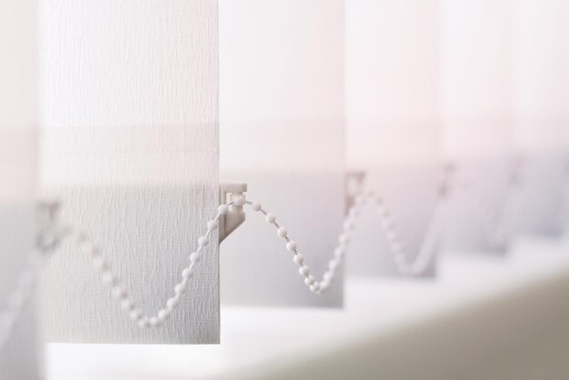 A row of white vertical blinds cover the sunlight from the window Close up