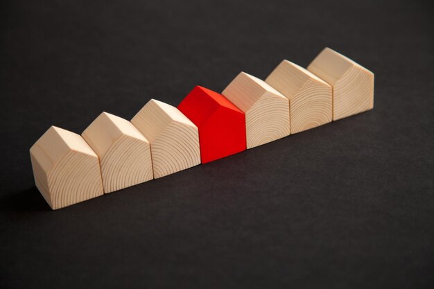 Row of wooden houses with a single red wooden house on dark background . Red wooden house standing