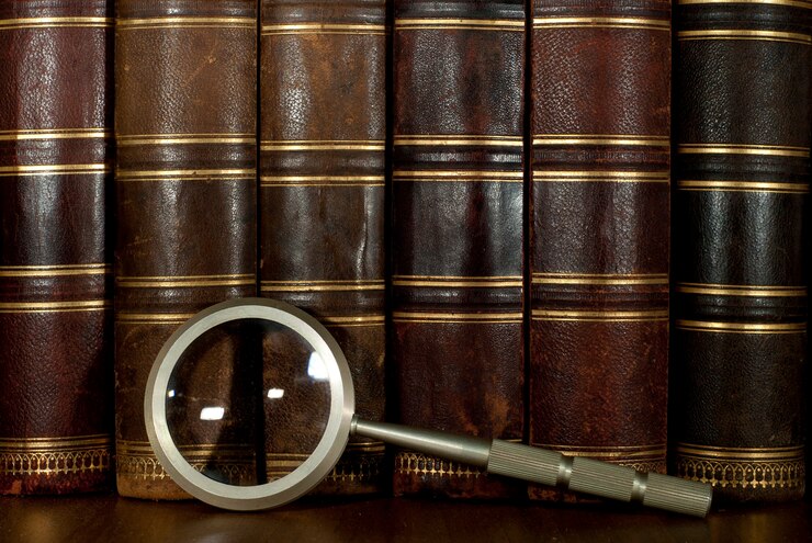 Row of worn leather antiquarian book spines with gold embossing and a magnifying glass