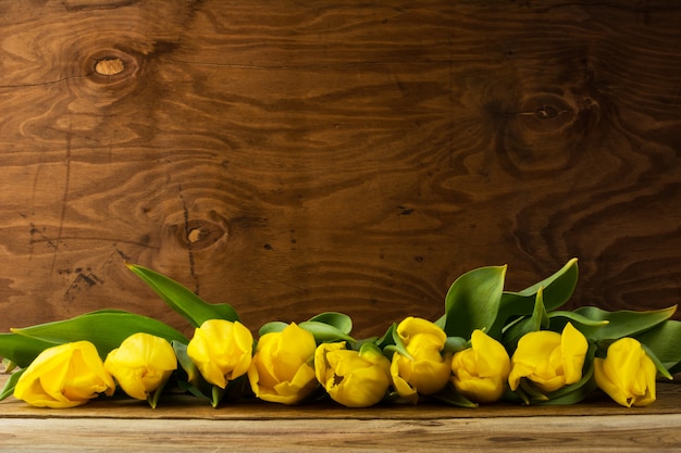 Row of yellow  tulips on wooden surface, copy space
