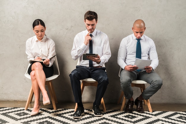 Photo row of young people sitting by wall while waiting for their turn for interview