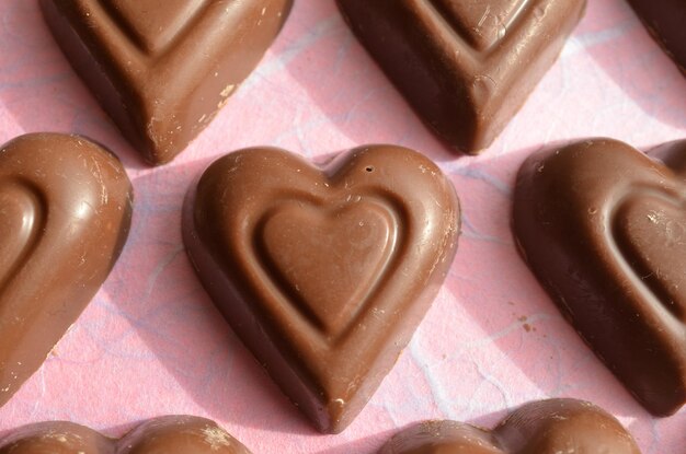 Photo rows of chocolate heart candy on pink paper